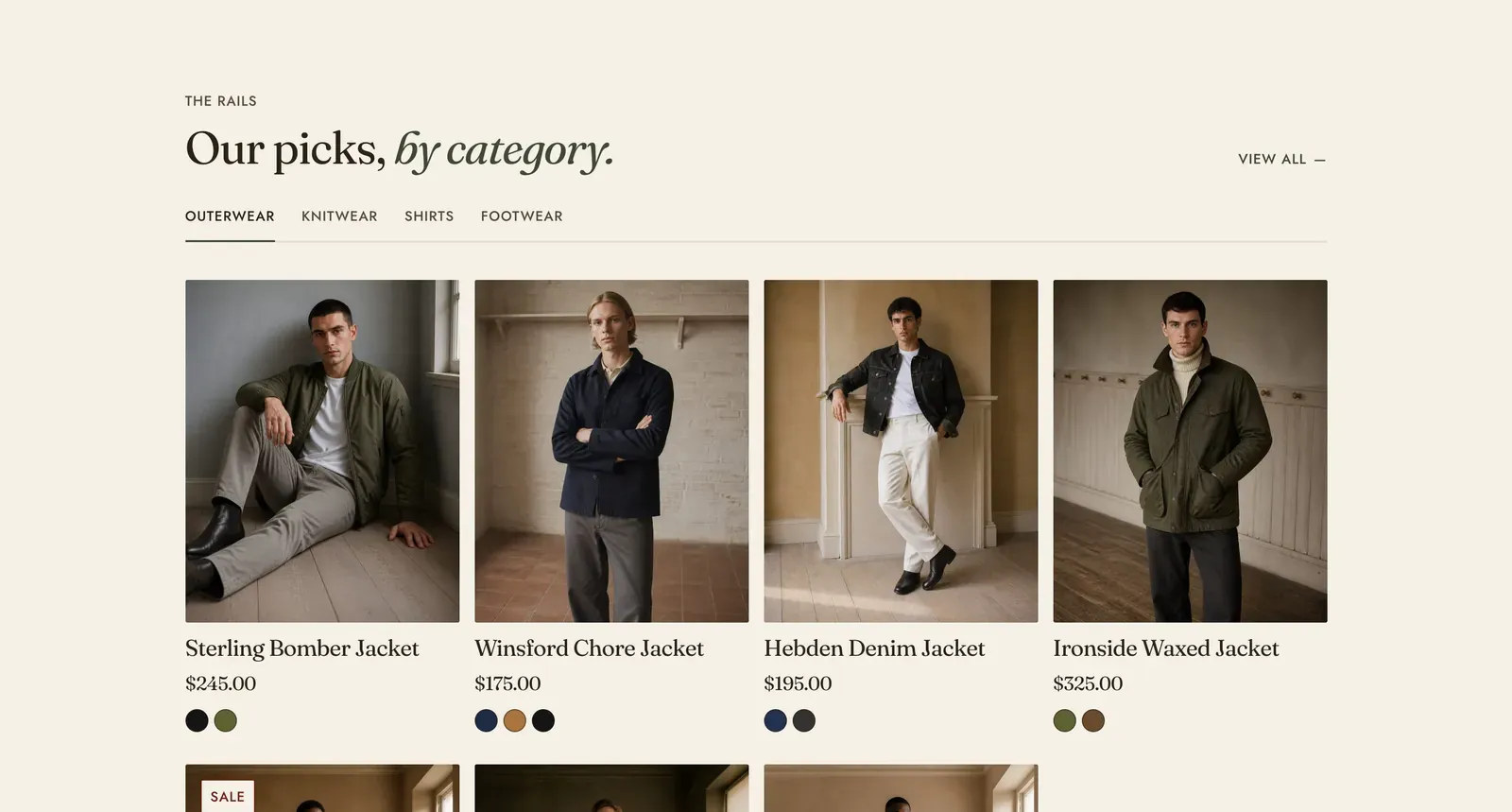 The Lapels Product tabs section: the label "The rails" over the heading "Our picks, by category." with the last two words in italic, a "View all" link at the right, tabs reading OUTERWEAR, KNITWEAR, SHIRTS and FOOTWEAR with the first marked, and a grid of product cards beneath reading Sterling Bomber Jacket $245.00, Winsford Chore Jacket $175.00, Hebden Denim Jacket $195.00 and Ironside Waxed Jacket $325.00, with a second row starting below.