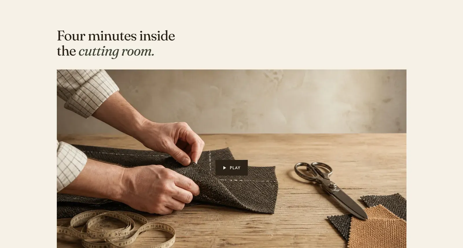 The Lapels Video section: the heading "Four minutes inside the cutting room." with the last two words in italic, above a photograph of a cutter's hands pinning dark herringbone cloth beside shears and a tape measure on a pale workbench, with a small dark PLAY button set over the center.